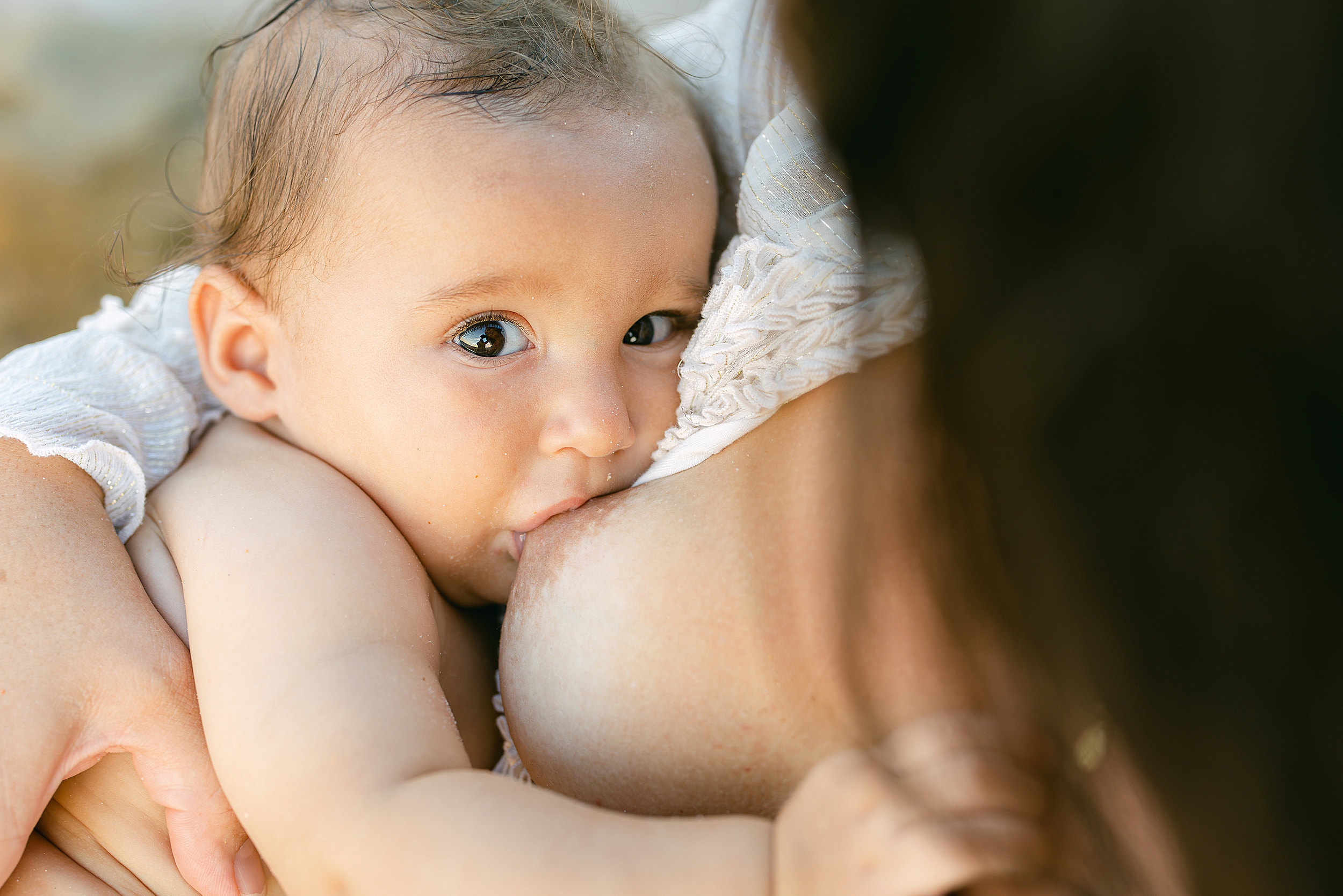 A mother breasts feeds her baby boy on the beach at sunset.