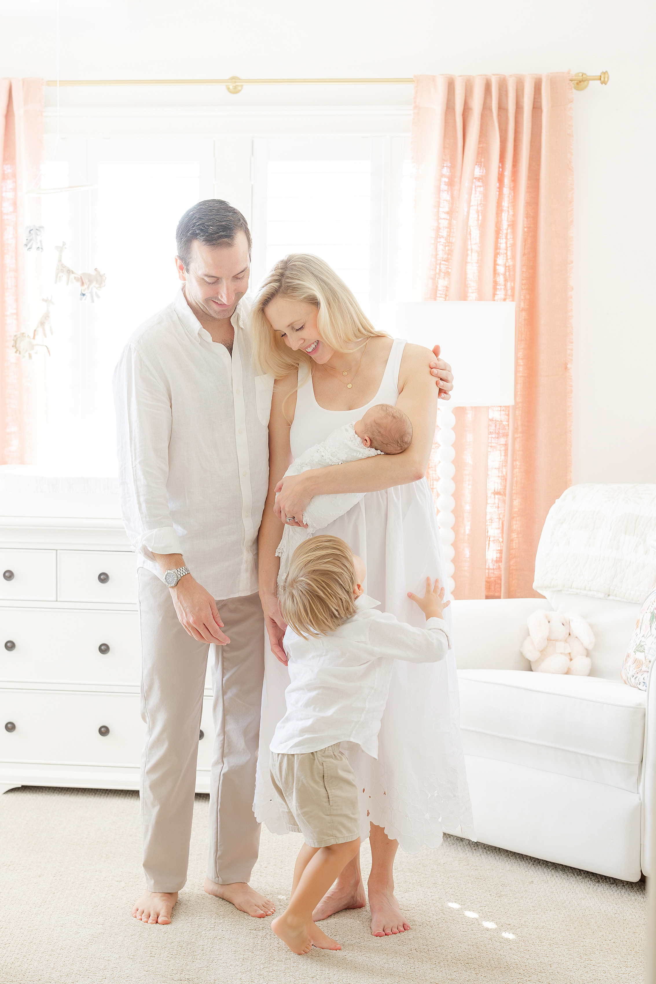 A family sits on the floor of their newborn baby girl's pink and white jungle themed nursery.