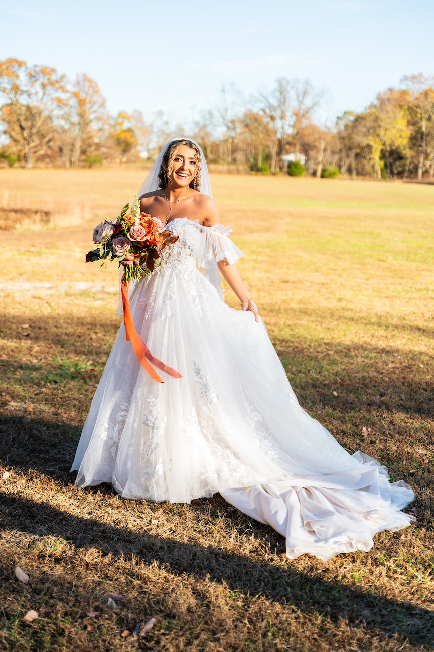 Fall bride at sunset smiling while holding her bouquet with orange ribbon