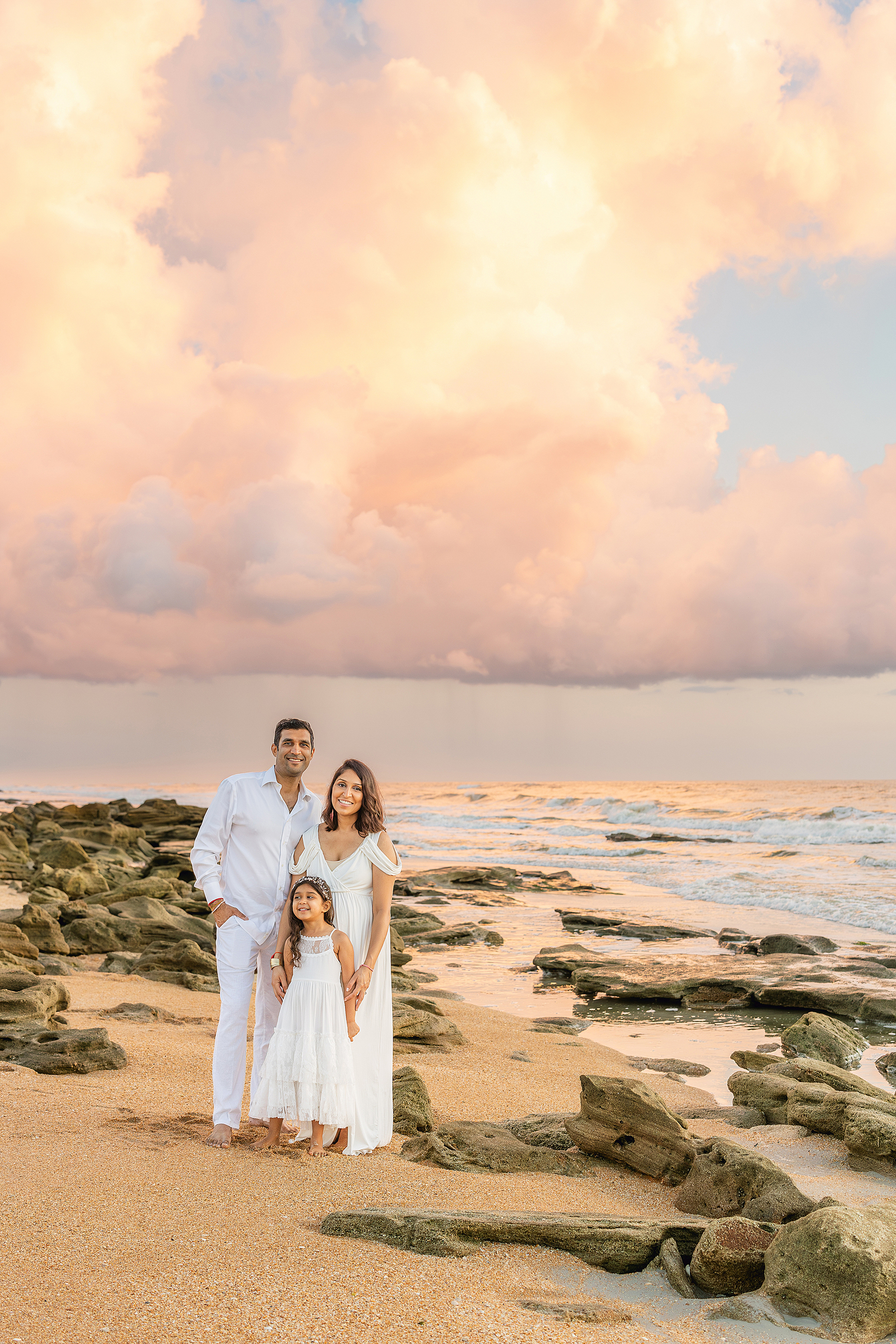 A colorful family portrait of a family of three standing on the beach at sunrise in Saint Augustine, Florida.