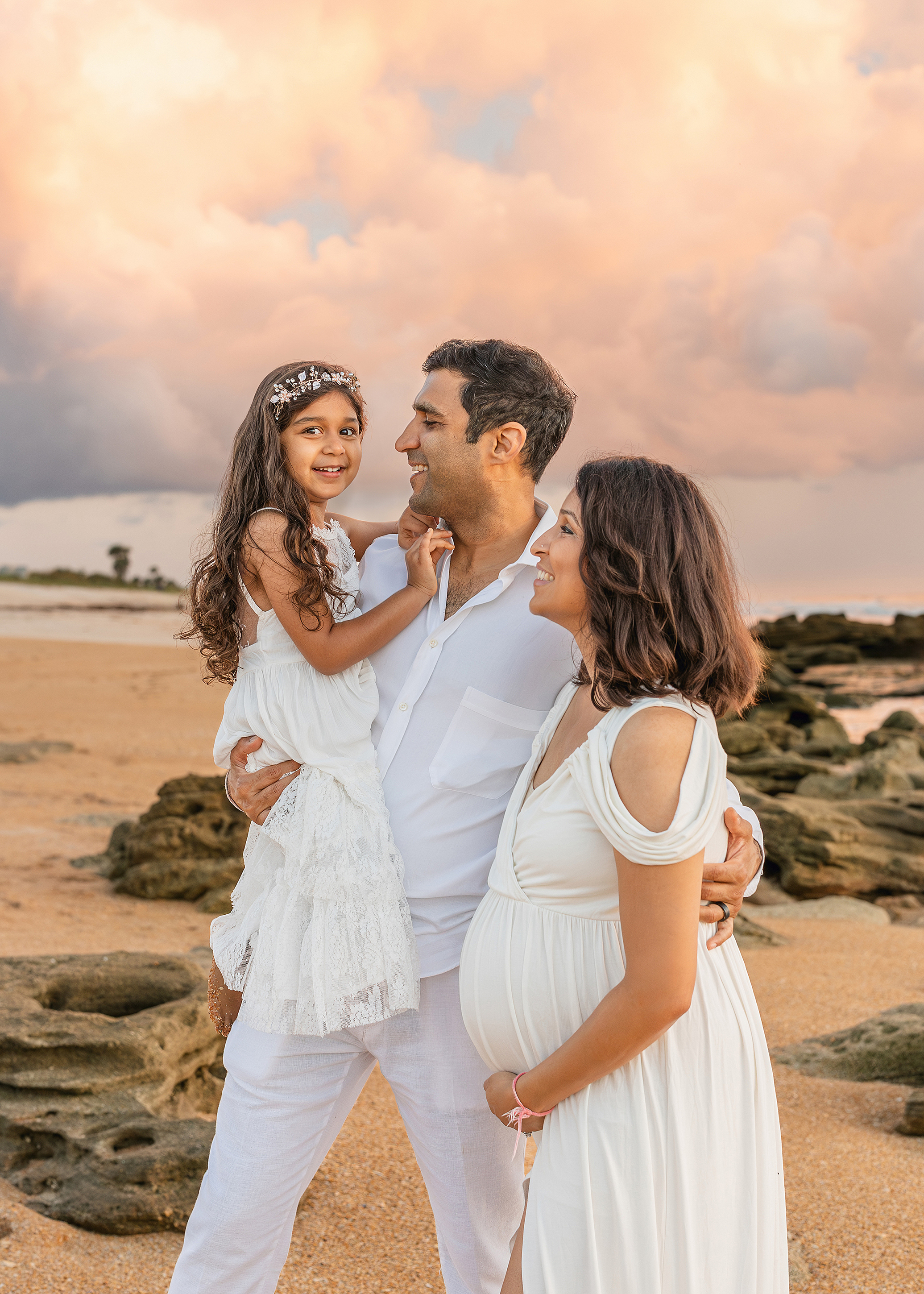 A colorful, pastel-hued family portrait of three people on the beach at sunrise.