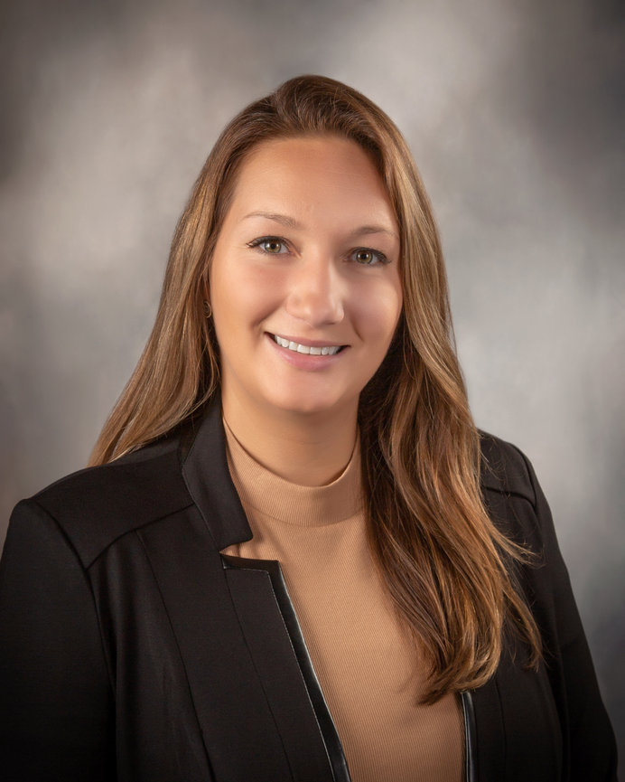 Professional woman in a blazer and tan turtleneck, smiling against a neutral background.