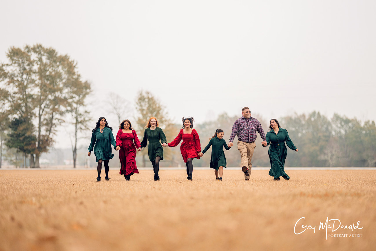 A group of people holding hands and walking in a field with trees in the background.