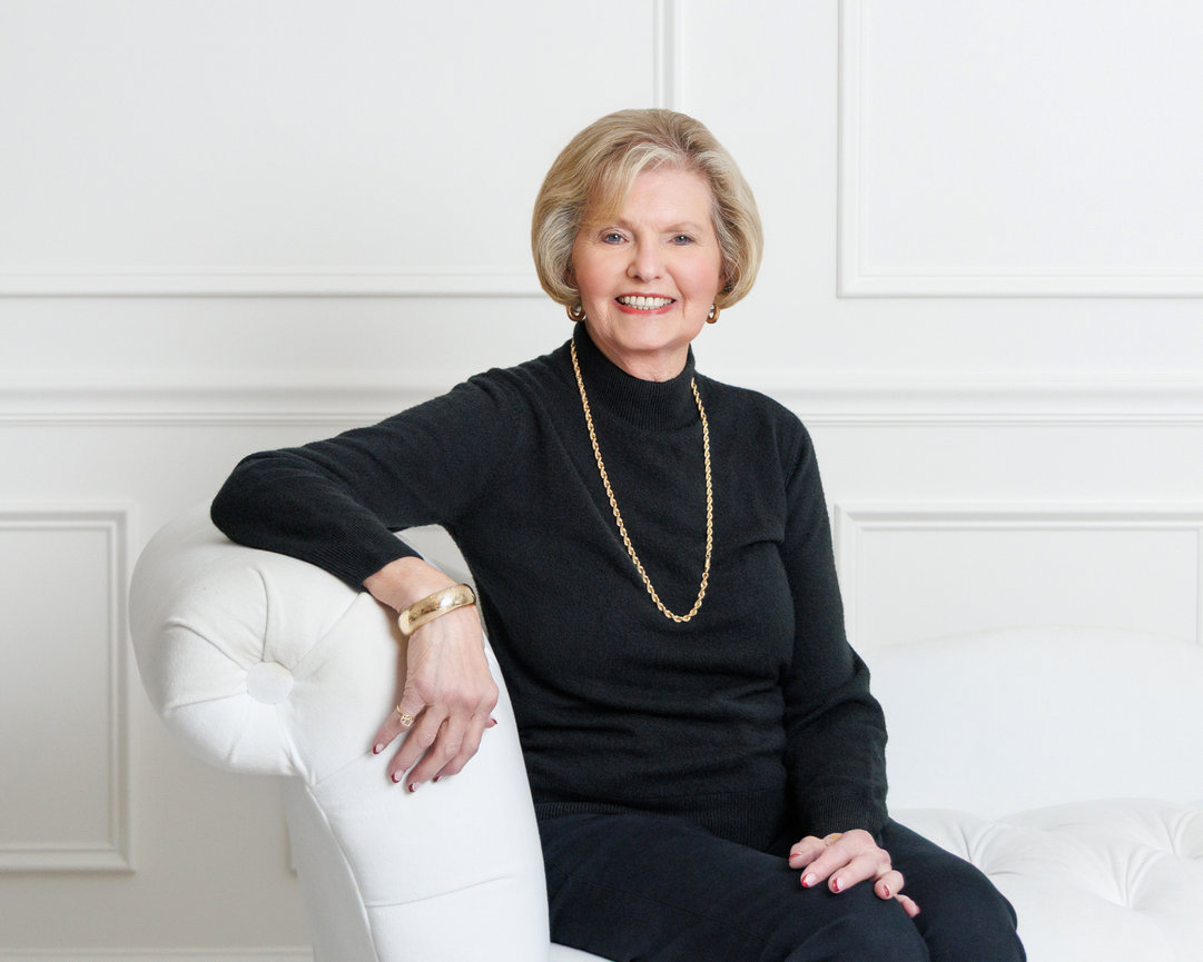 Smiling woman in black sweater sitting on a white sofa in a bright room.
