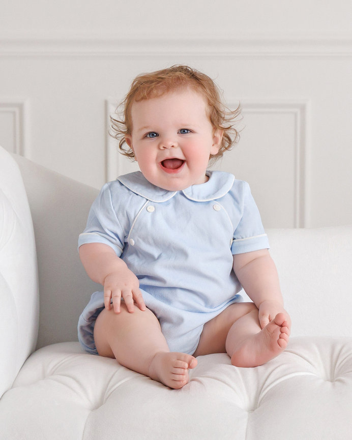 Smiling baby in a light blue outfit sitting on a white chair.