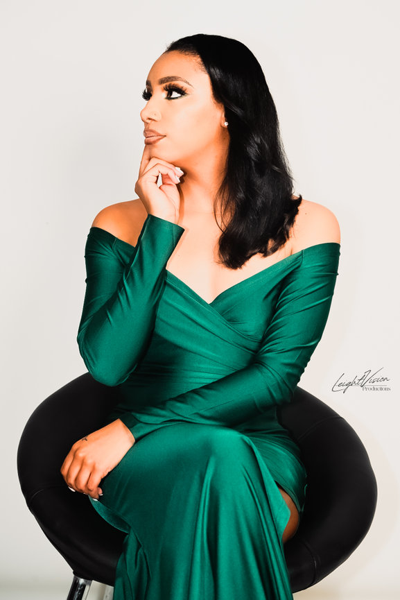 A woman wearing a green dress sits on a chair, showcasing a serene and stylish demeanor.