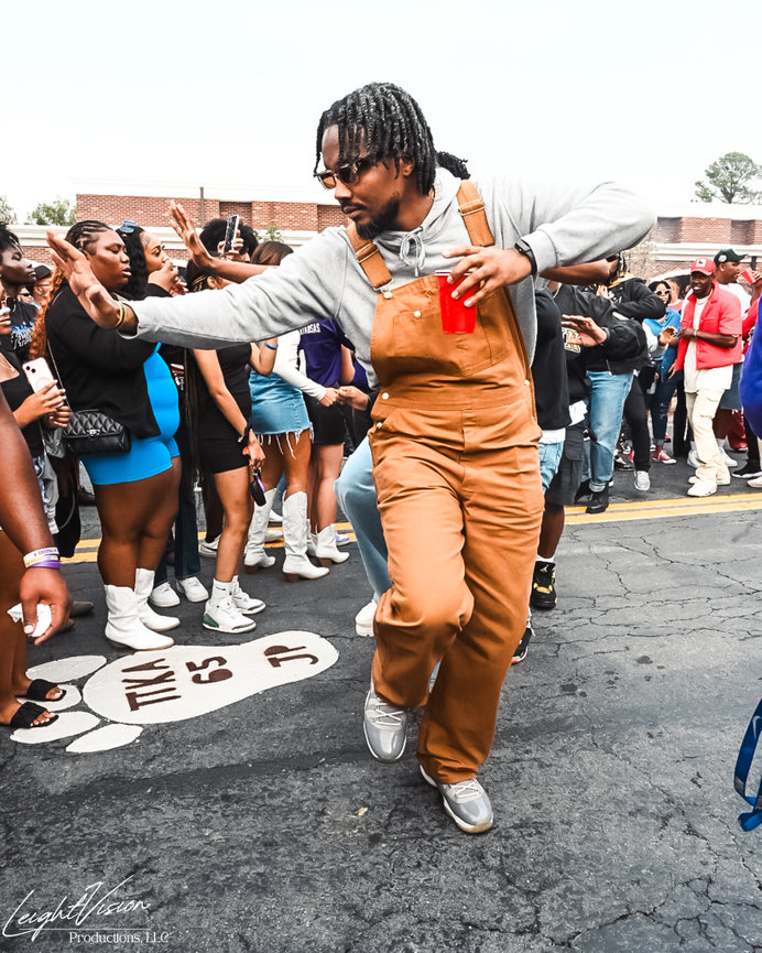 A man wearing overalls performs a dance in front of a cheering crowd, radiating joy and excitement.