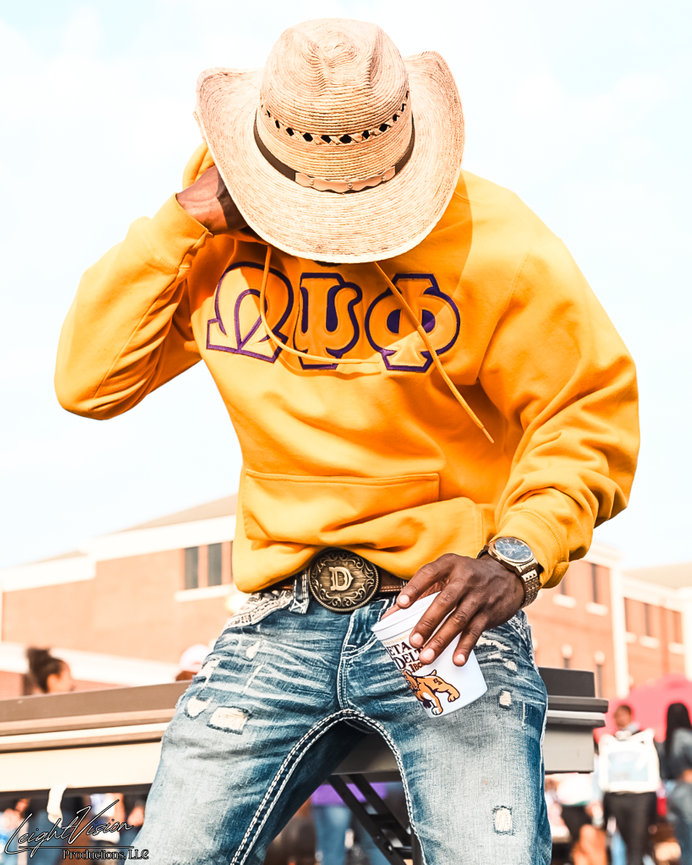 A man dressed in a yellow sweatshirt and jeans sits on a bench, taking a break in a serene outdoor environment.