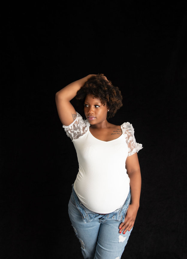 Pregnant woman in a white top with lace sleeves poses against a black background.