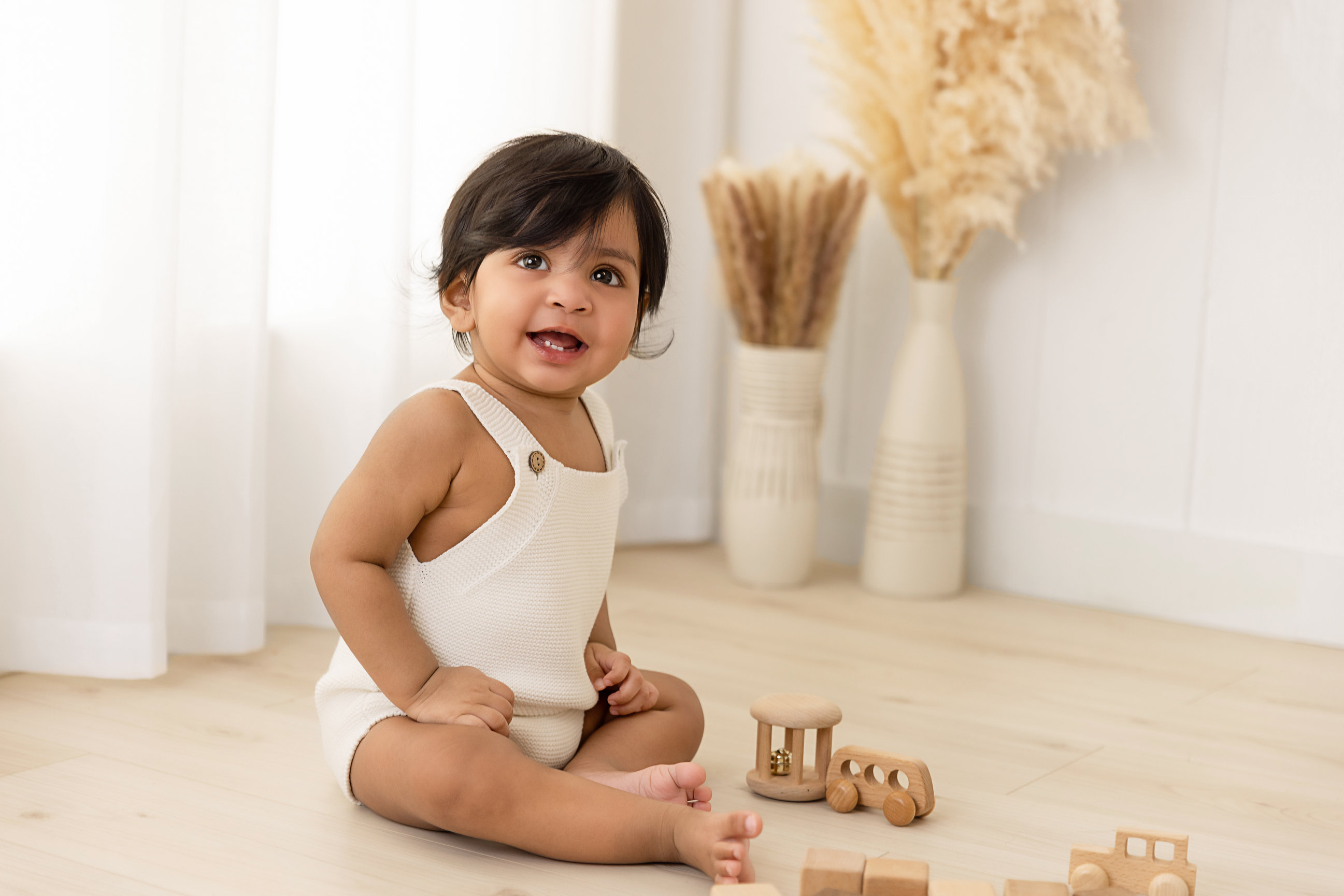 Smiling one-year-old in a cream outfit playing with wooden toys in the lifestyle area