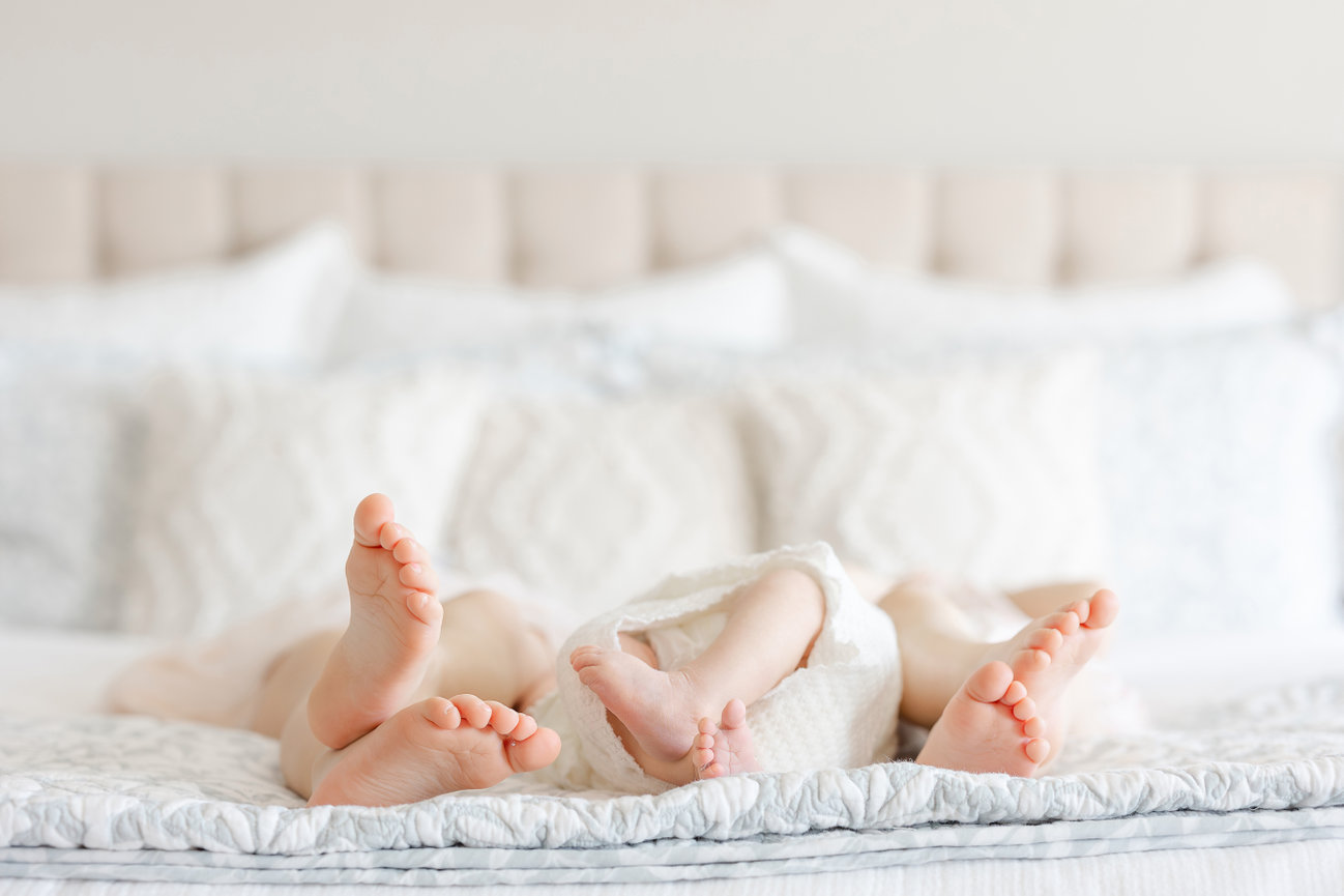 Lifestyle newborn session at home with three children's feet on the bed.