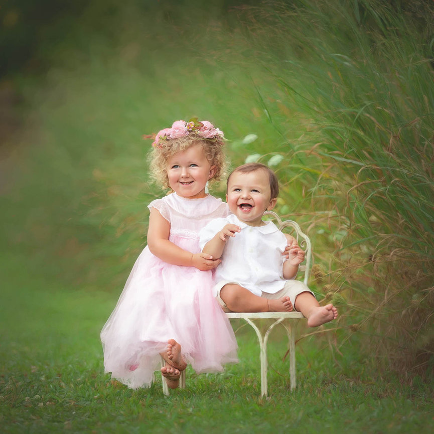 Candid portrait of two young siblings laughing together outdoors, captured in soft golden light.