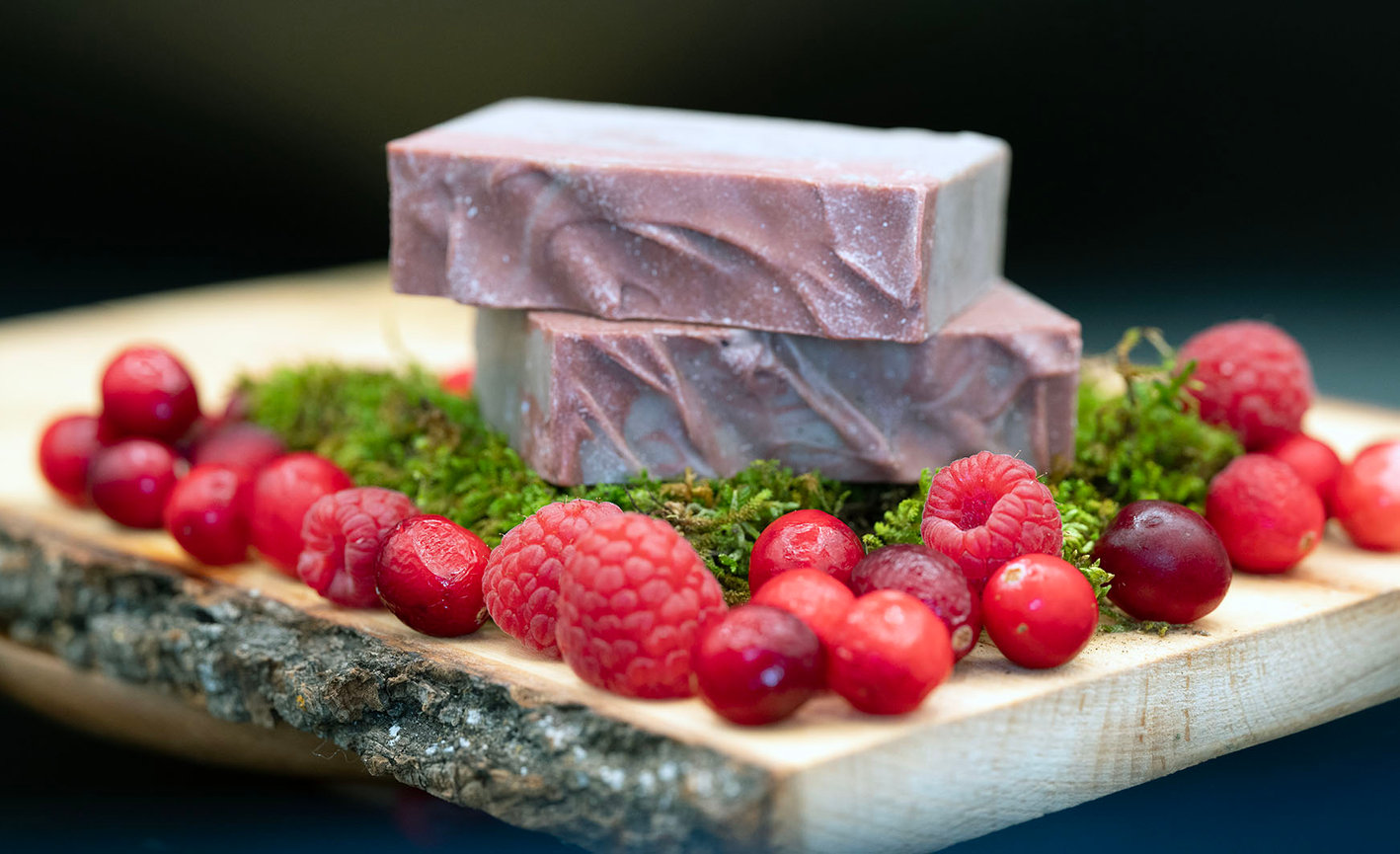 Artisan berry soap bars with raspberries and cranberries on a rustic wooden board