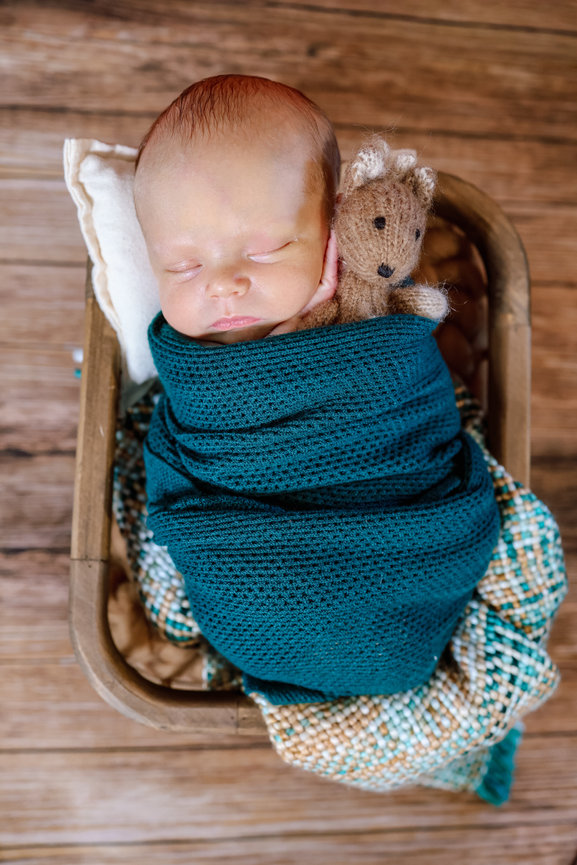 Sleeping newborn swaddled in teal wrap inside a small basket