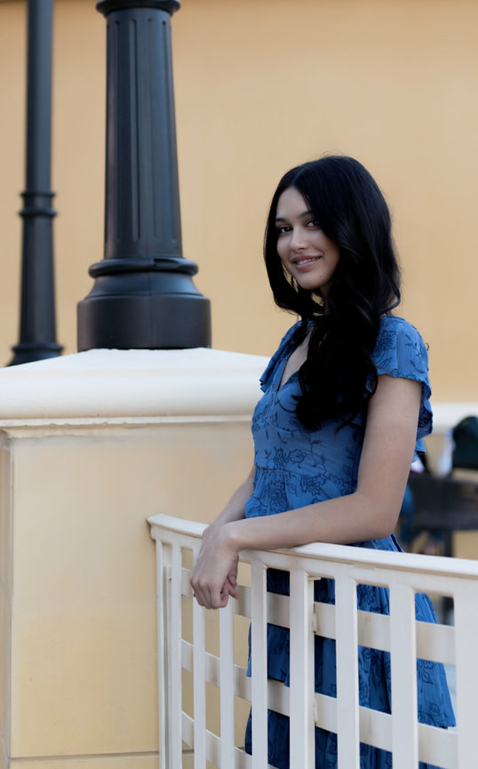 Woman in a blue dress posing casually outside against a pale backdrop