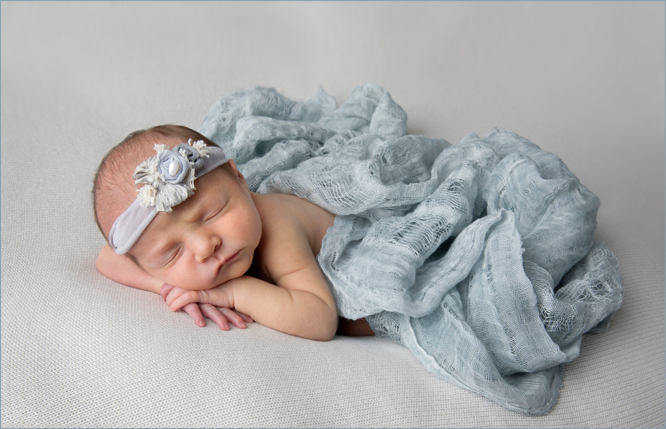 Newborn sleeping wrapped in a blue blanket with a headband