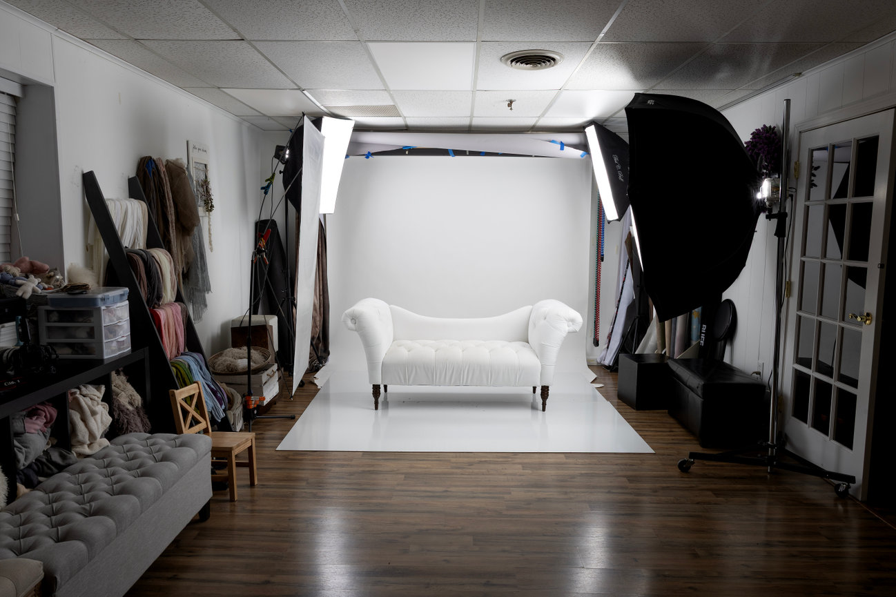 White couch minis studio setup with a white backdrop, a white sofa, and professional lighting equipment at Paula Swift Photo studio.