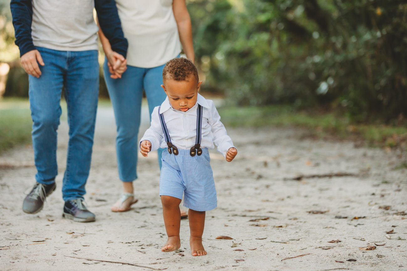 Adorable barefoot toddler leading parents at Lake Mills Parks in Chuluota Florida.