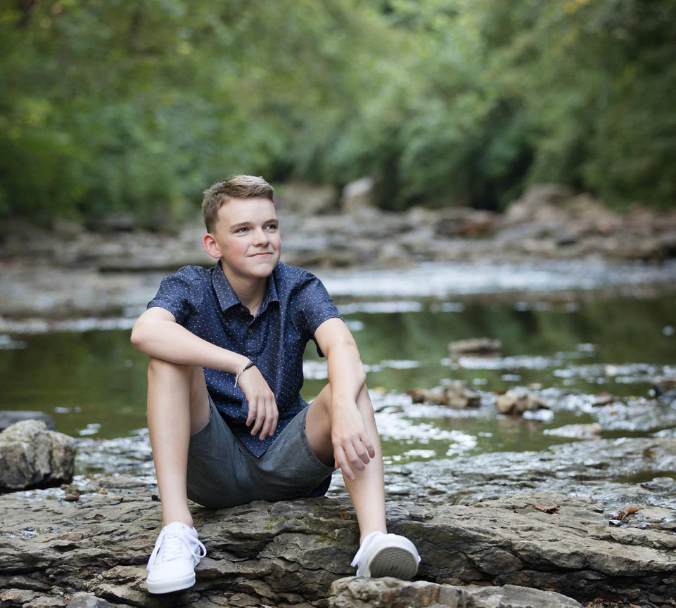 Young man sitting by a flowing stream outdoors