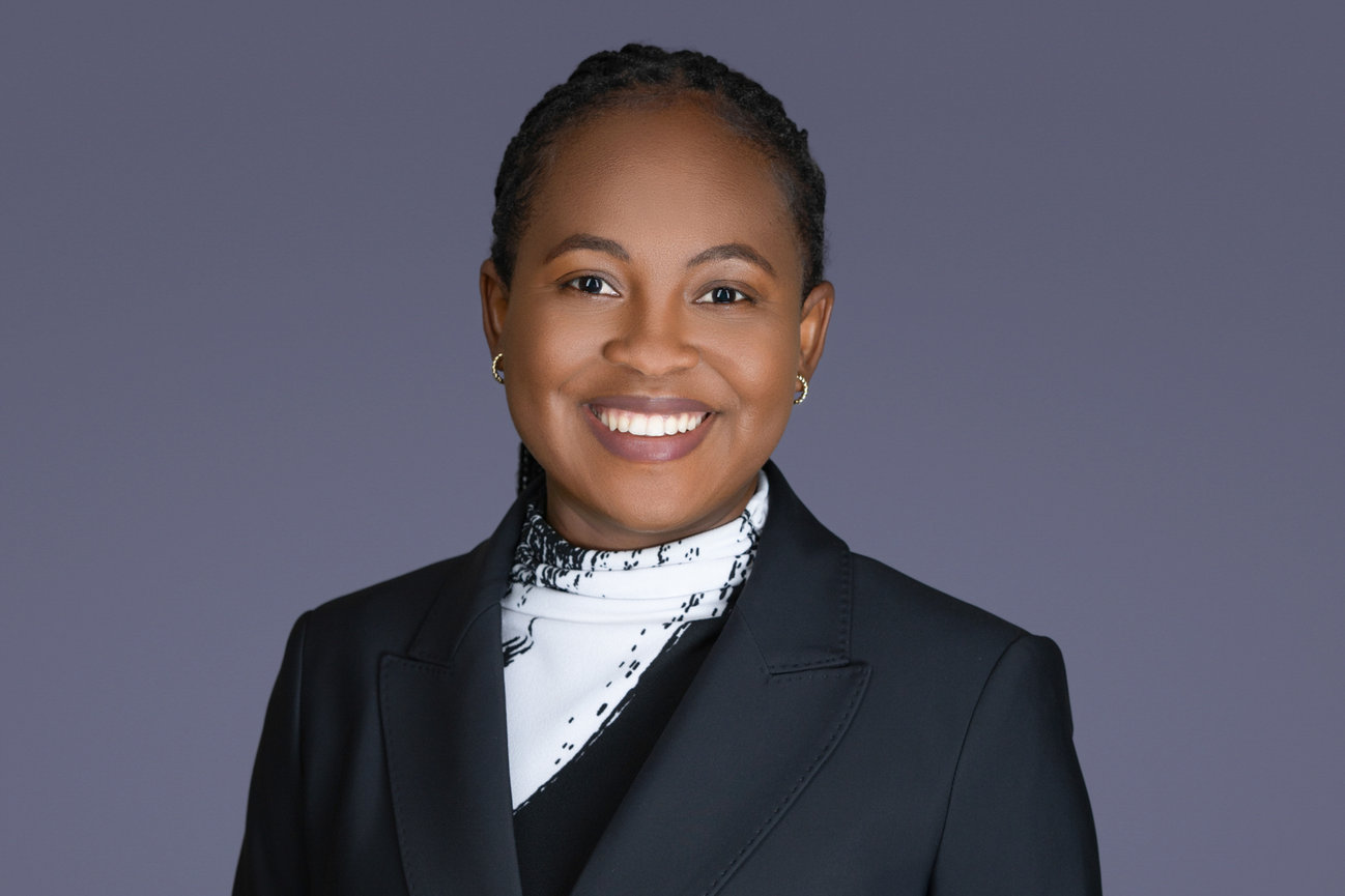 Professional headshot of a smiling woman in a dark blazer against a gray background