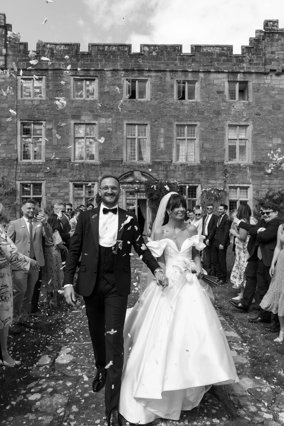 Black & White images of a bride and groom celebrate their wedding, walking outside Askham Hall as guests shower them with confetti.