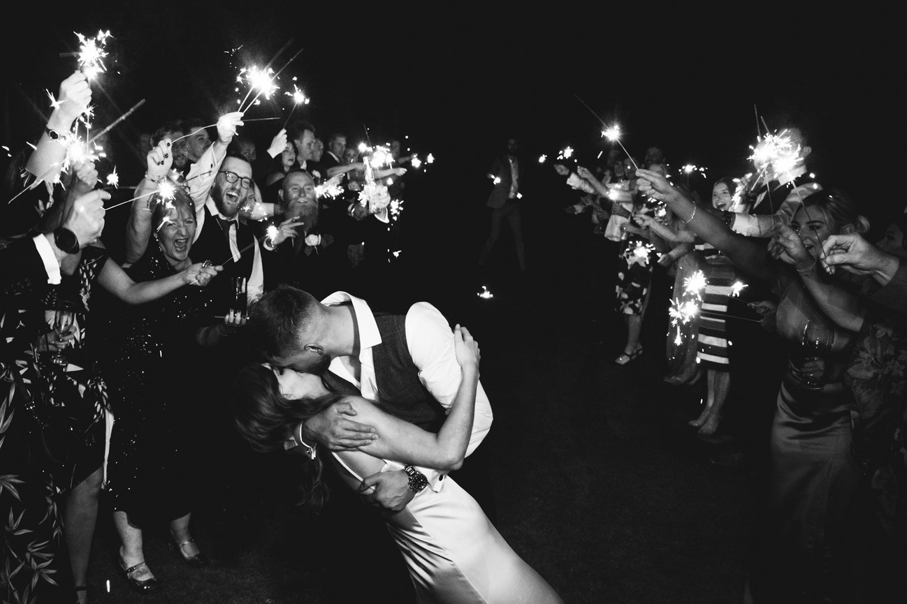 Monochrome Flash photography: Sparkler exit at Hawkstone Hall, guests celebrate while bride and groom share a Hollywood kiss.