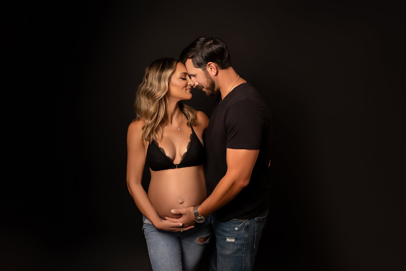 Intimate couples maternity session with mom in a black bra, jeans, and exposed bump.