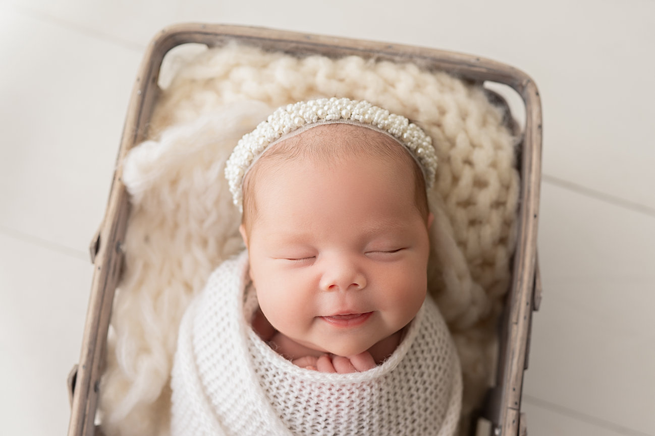 Newborn swaddled in earth-toned knit wrap and posed in distressed picnic basket with subtle textured backdrop