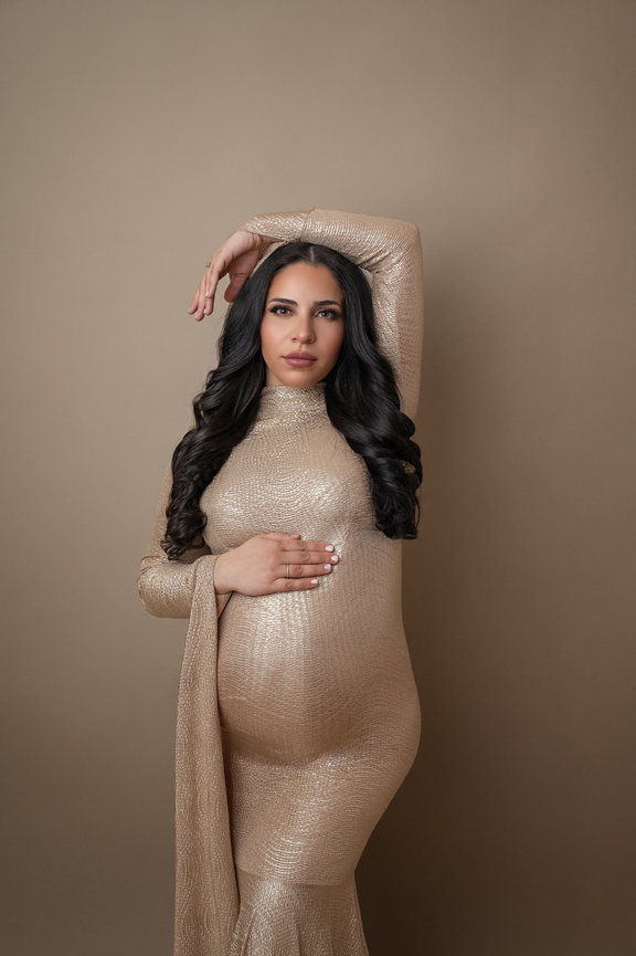 Elegant pregnancy photo of mother-to-be in flowing couture gown with soft side lighting
