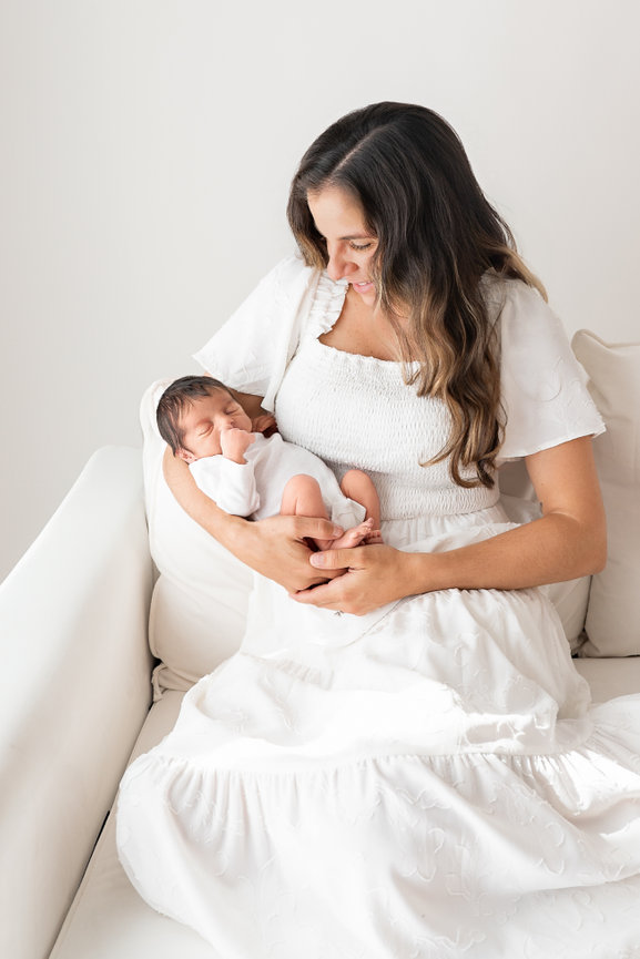 Emotional moment with mom looking at baby on white couch in Toms River lifestyle studio
