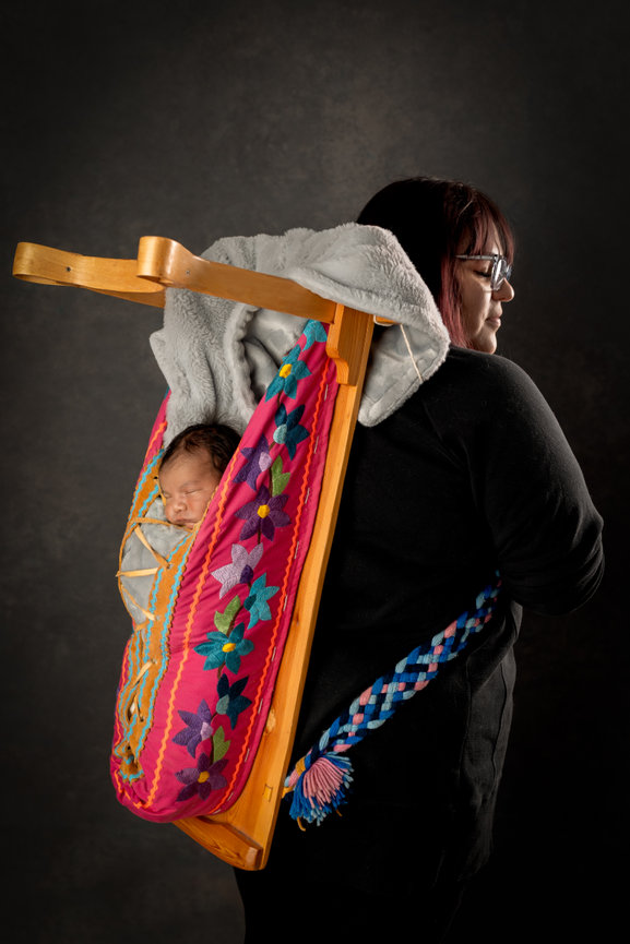 Woman carrying a newborn in a traditional textile baby carrier on her back, with a cozy blanket.
