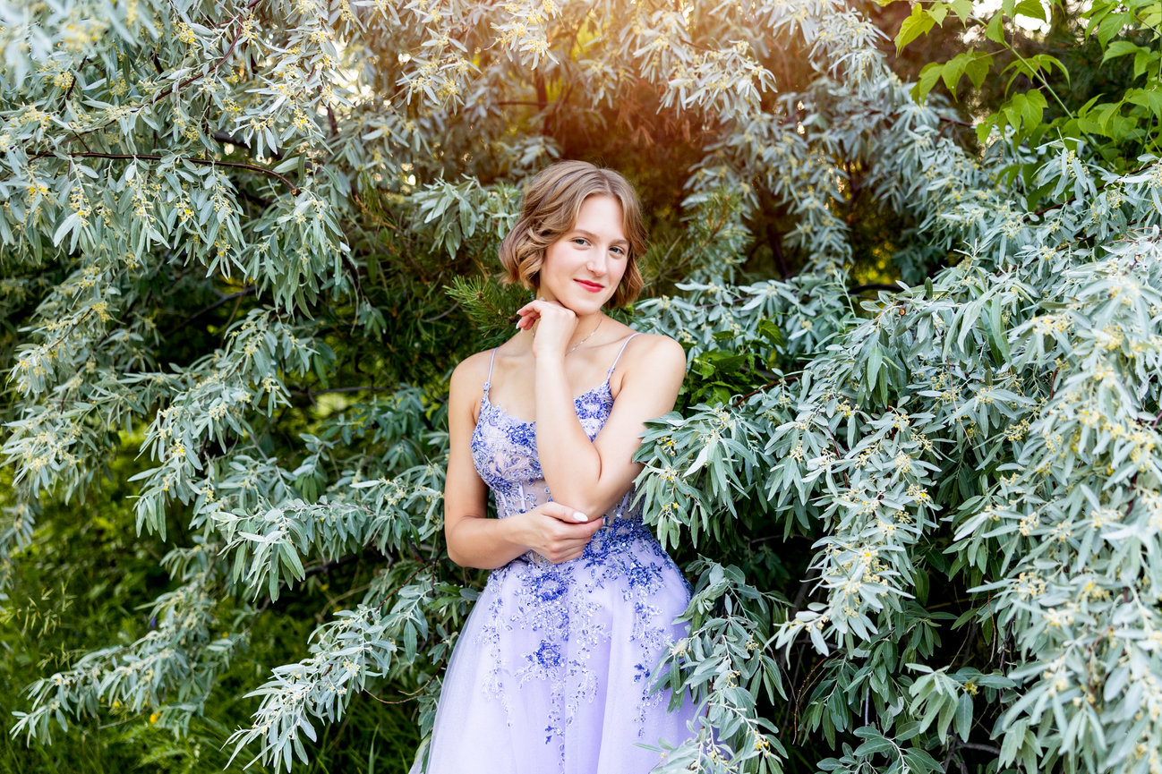 Woman in floral purple dress standing among lush green foliage.