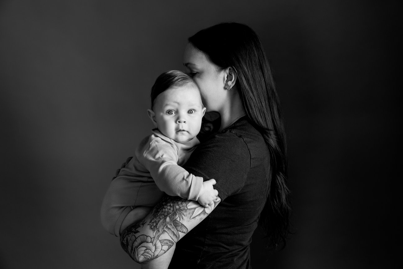 Mother holding baby in arms, both facing forward, in black and white portrait.