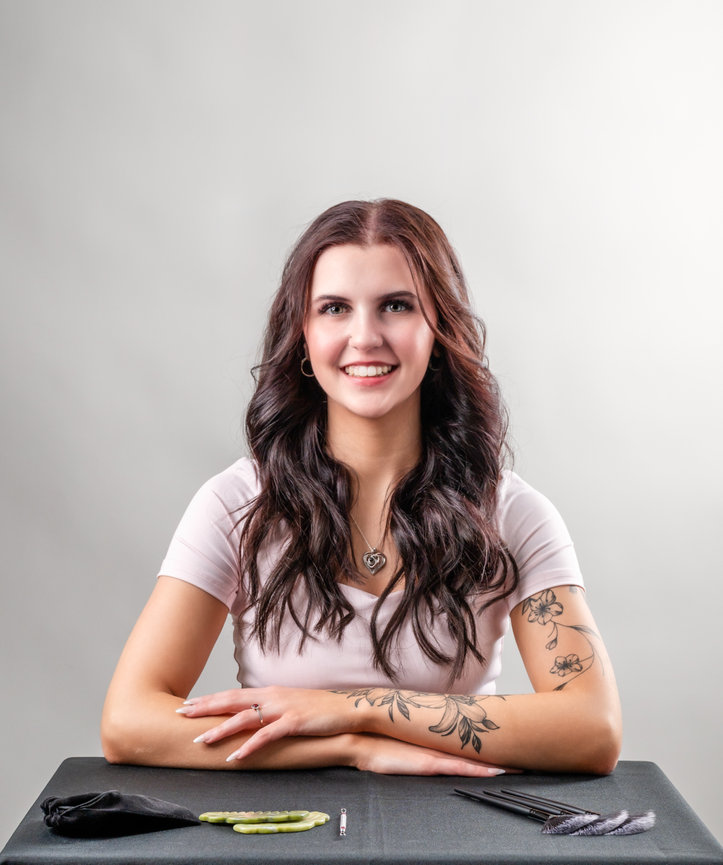 Woman in pink shirt sitting down at table with beauty tools in front of her looking at the camera smiling