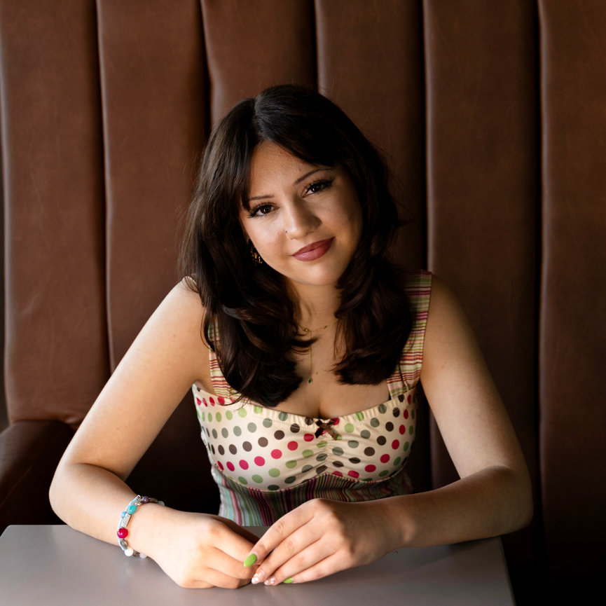 Portrait of a teen girl sitting at a table with a brown upholstered backdrop