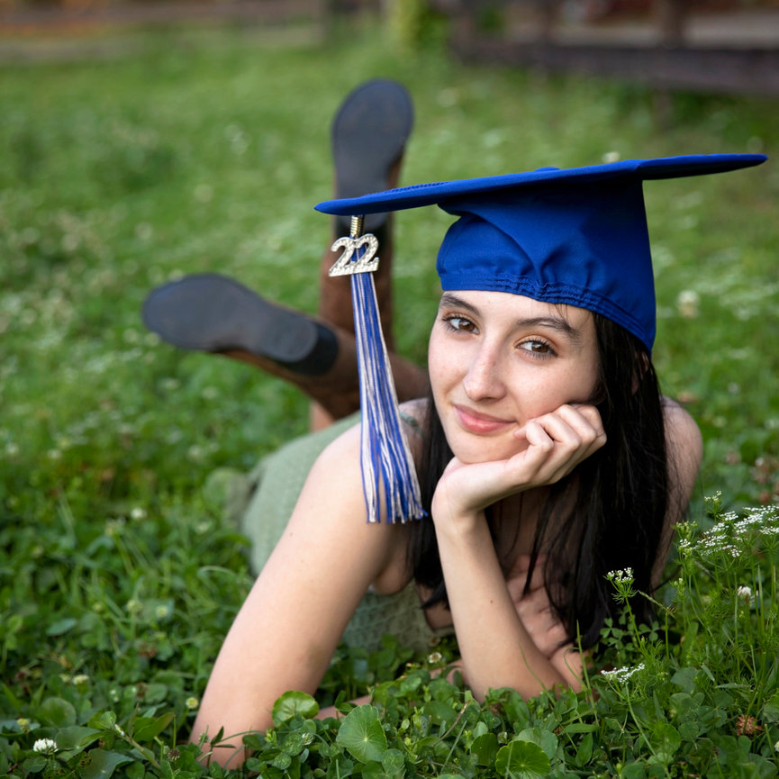 Young woman in blue graduation cap lying in grass outdoors