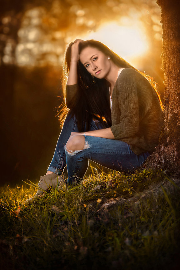 Woman sitting on a grassy slope with warm backlight.
