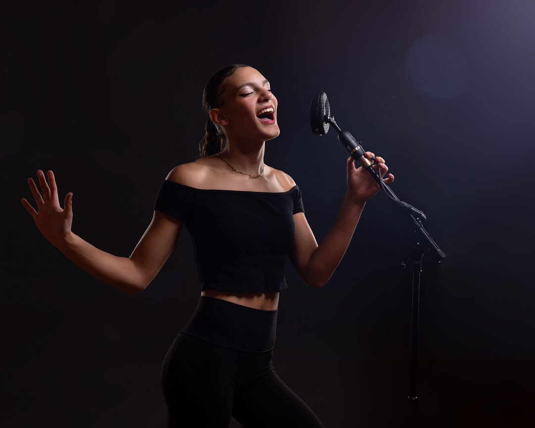 Artistic portrait of Musical Theater singer singing into microphone on dark background with strong lighting