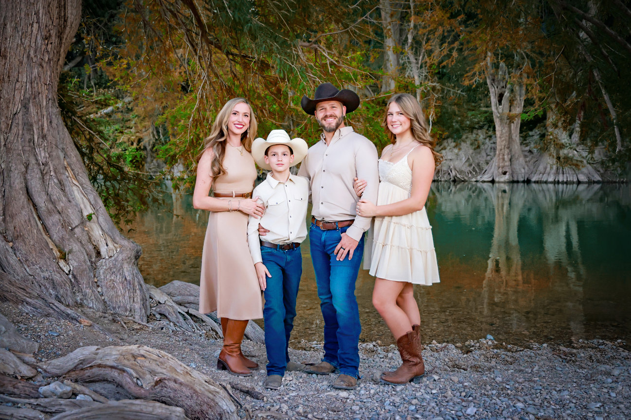 Family portrait by a riverbank, with two women, a man in a cowboy hat, and a boy in western clothes