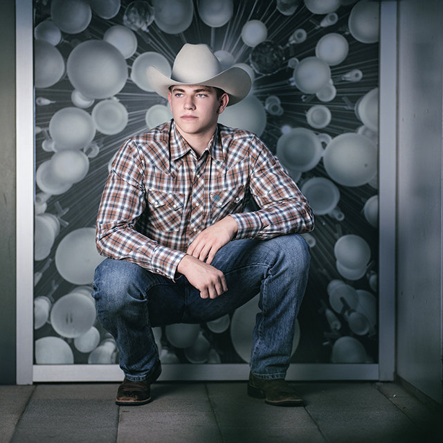Senior boy in cowboy hat sitting on bench in city of Phoenix setting