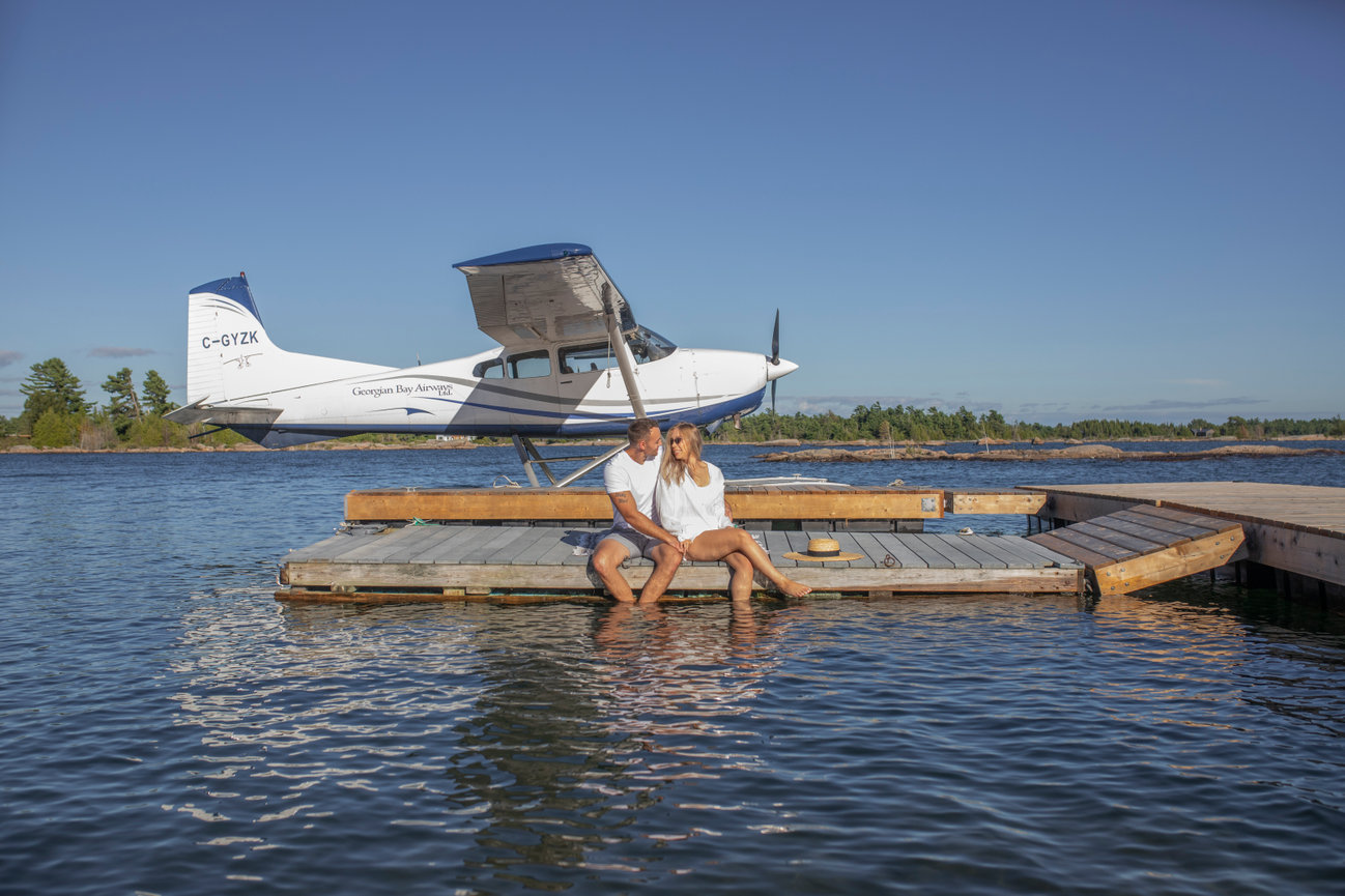 Couple sitting on dock with seaplane in the background