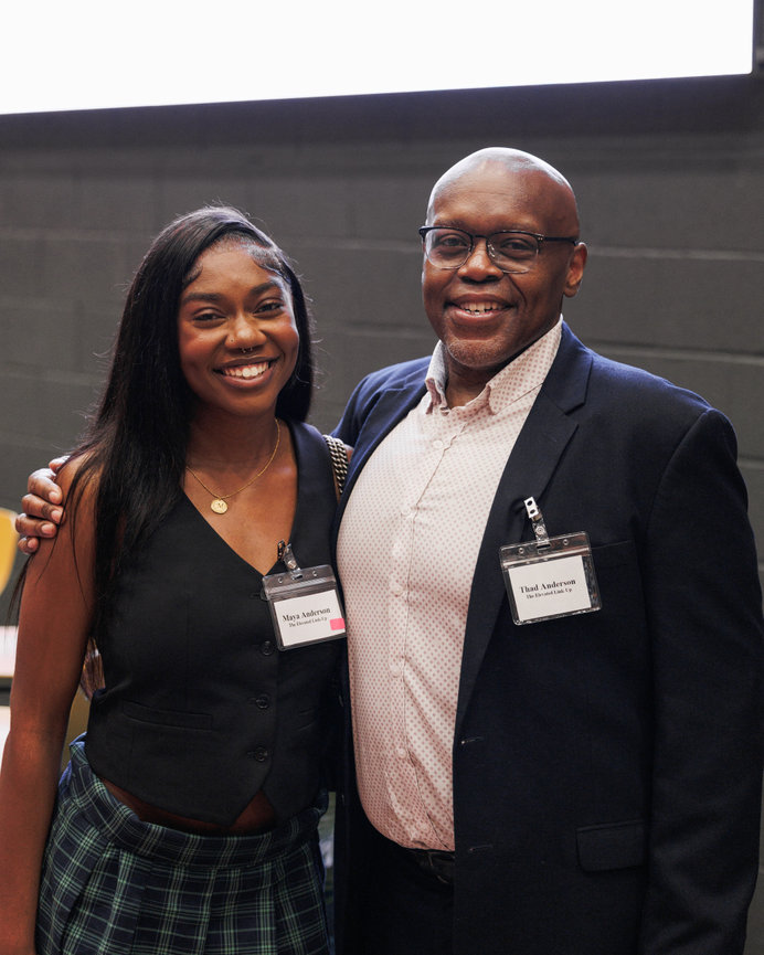 Event photography of a smiling woman in a green dress and a man in a blazer wearing event name badges