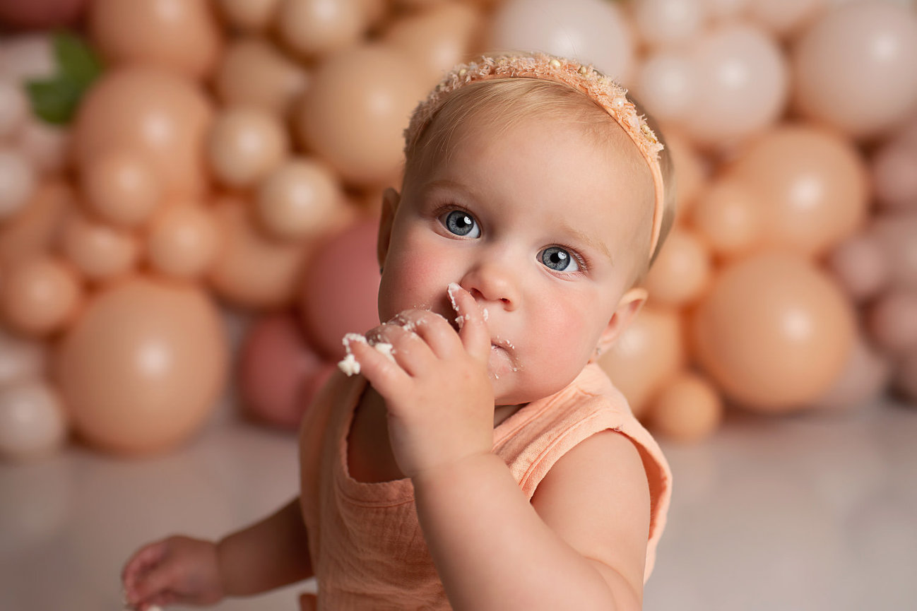 Baby girl eating cake during first birthday cake smash photoshoot with Kansas City baby photographer Dreamworks photographer