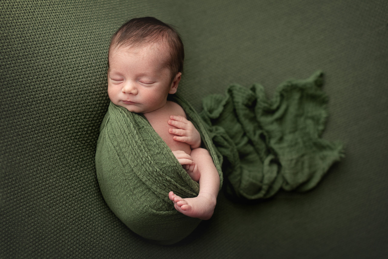 A sleeping newborn boy wrapped in a soft green blanket, looking peaceful and cozy during his newborn photography session with Catherine Whitney Photography.