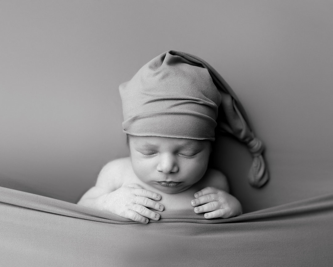 Black-and-white photo of a sleeping baby wearing a knitted hat, resting on a soft blanket.