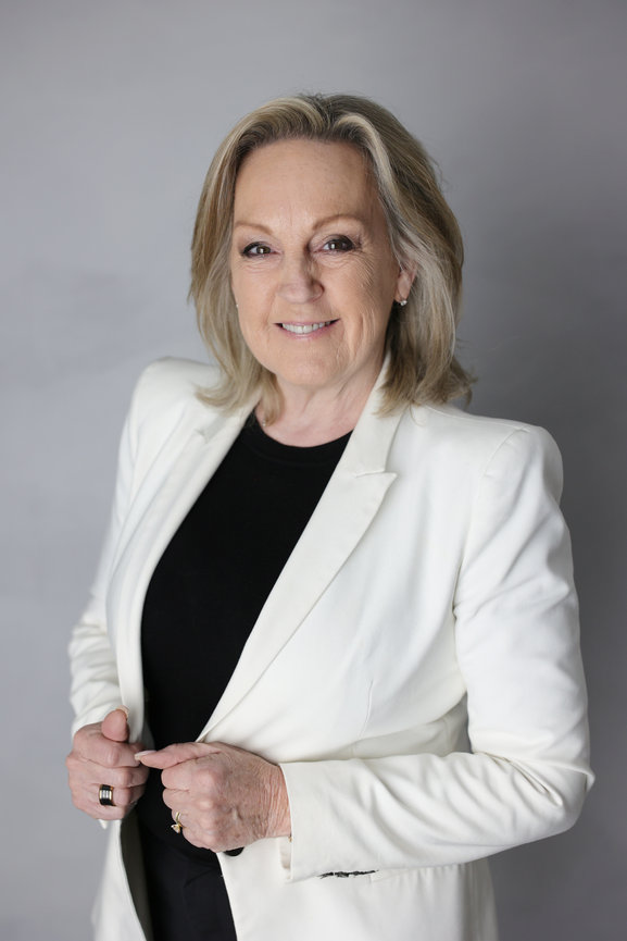 Portrait of a smiling woman in a white blazer and black top against a gray background. personal branding photos Melbourne