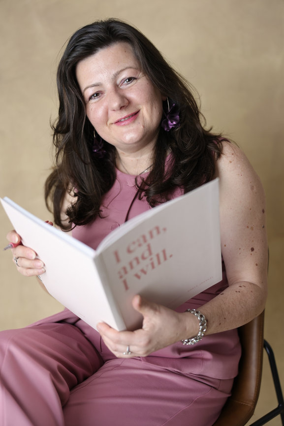 Woman in pink holds an open book and smiles at the camera. authentic photos for my business and website