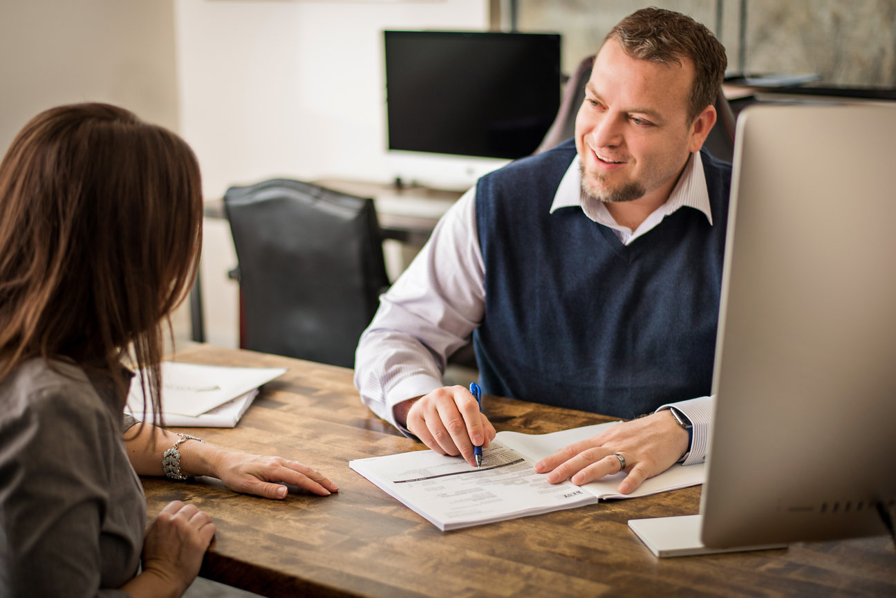 Man sitting across from a woman at a desk going over paperwork.