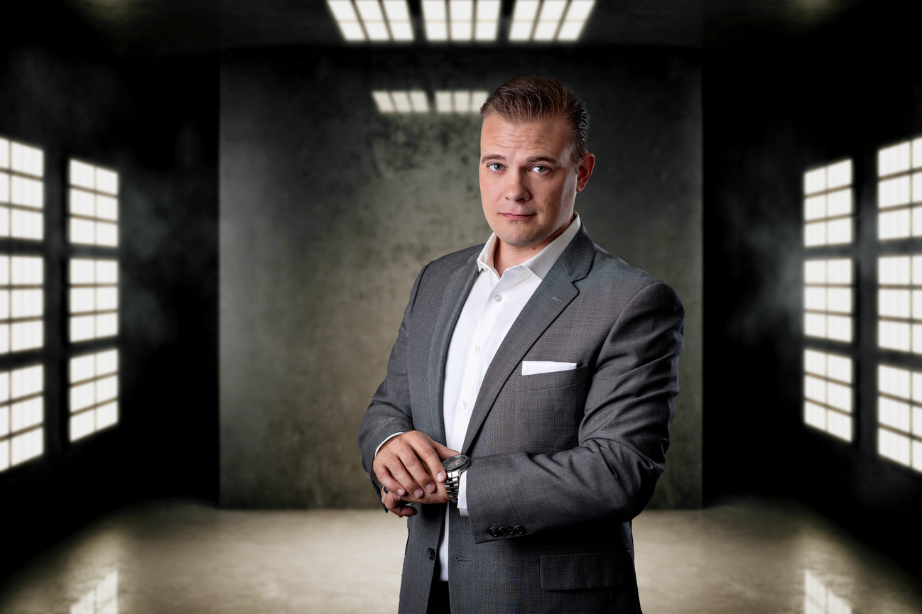 A man in a suit posing for a headshot in an industrial room with lights on the walls.