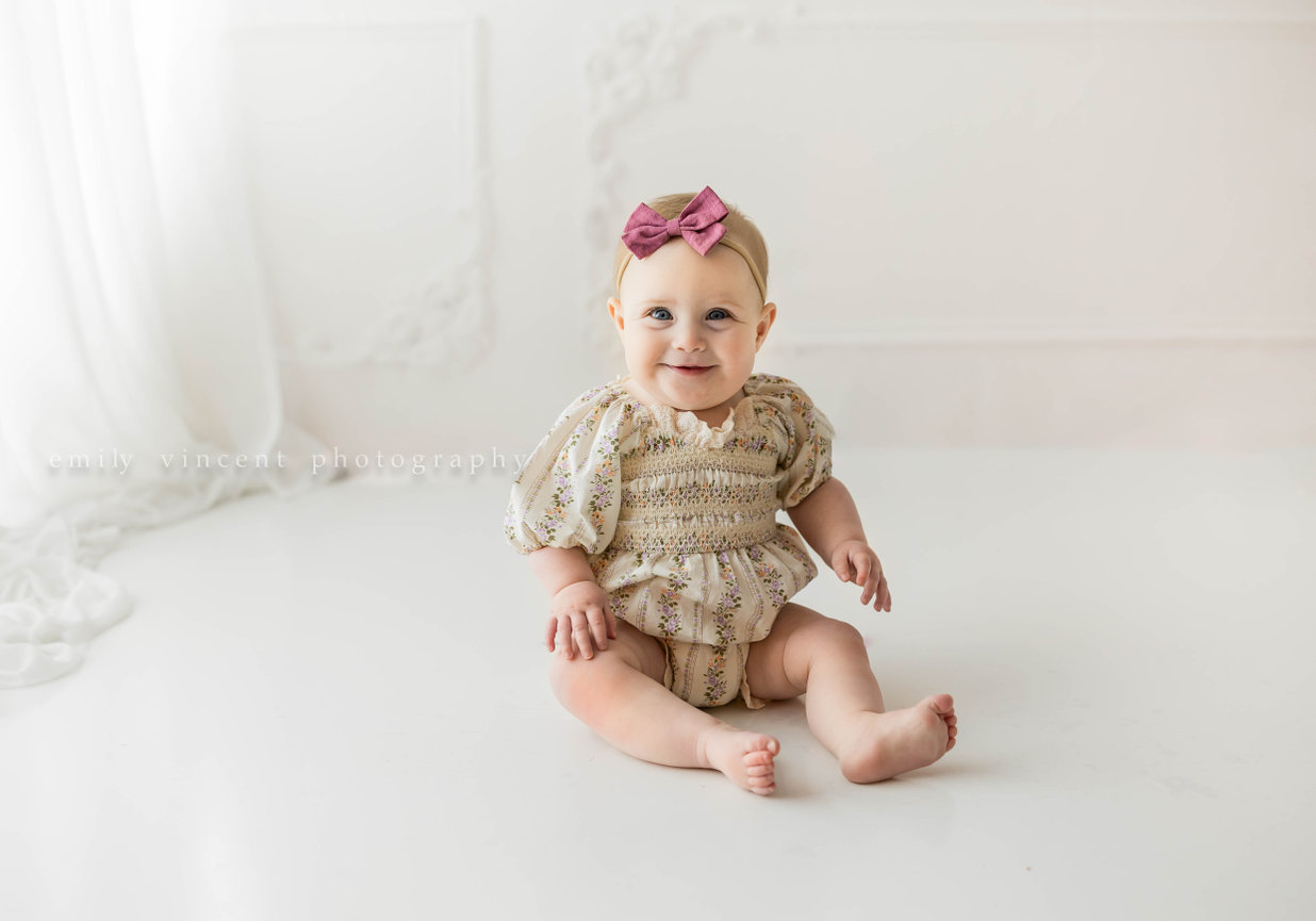 Milestone portrait of baby smiling and sitting on floor of neutral indoor photo session background